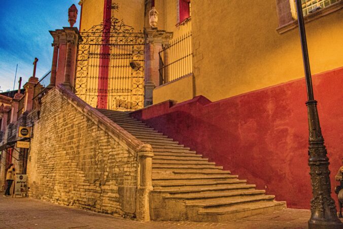Abendstimmung in einer kolonialen Altstadt von Mexiko mit farbenfroher Fassade, steinerner Treppe und kunstvoll verziertem Eingangstor in Guanajuato.